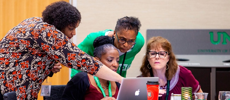 A group of women gather around a computer during NewsTrain training.