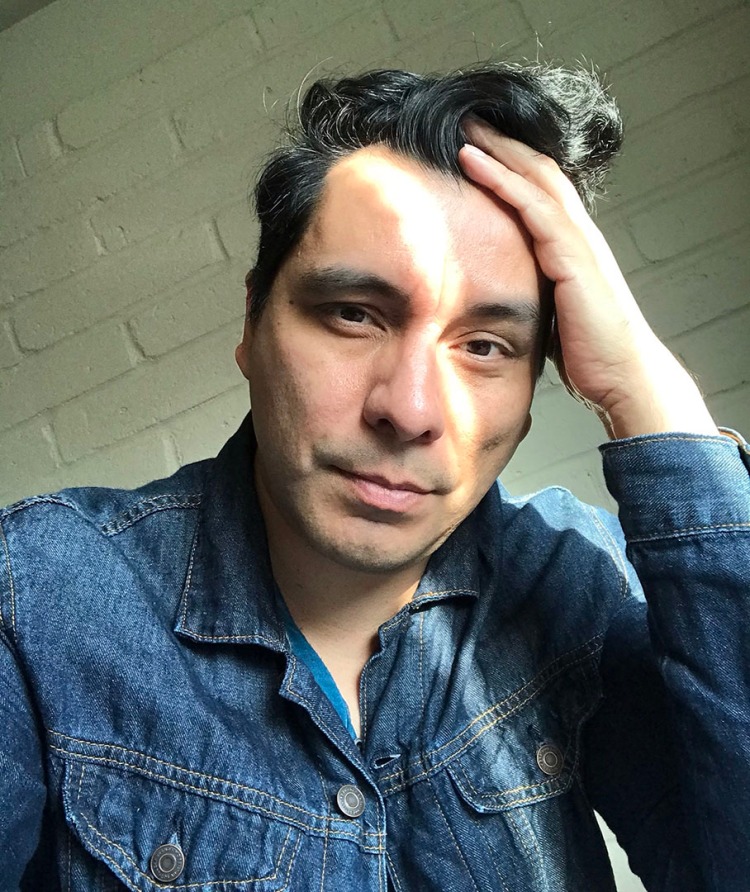 Manuel Muñoz in a blue denim jacket and left hand in his hair. Photo by Manuel Muñoz